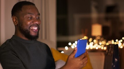 Wall Mural - Young positive african american video chatting with friends on smartphone in evening, tracking shot, empty space