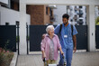 Leinwandbild Motiv Caregiver walking with senior woman client in front of nurishing home.