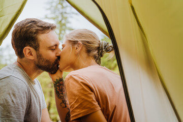 Wall Mural - White young couple kissing and hugging each other by tent in forest