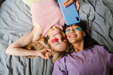 Wall Mural - Two multiracial girls in eye patches taking selfie on mobile phone