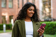 © Drobot Dean - Brunette indian woman using mobile phone while walking on city street