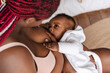 Young african american woman breastfeeding her baby in bedroom