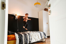 Playful Boy Jumping On Bed In Bedroom