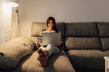 Happy Woman Using Laptop On Sofa In Living Room At Home