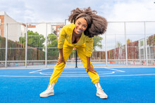 Happy Young Woman With Afro Hairstyle Bending On Sports Court