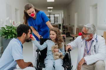 Happy doctors with clown red noses taking care about little girl.