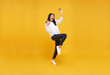 Happy young asian teen woman celebrating with mobile phone isolated over yellow background.