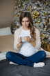 © Елена Бабанова - Pregnant woman with a mug of tea on Christmas morning sits on a bed in a cozily cosy bed in the bedroom alone in the afternoon. Concept: Christmas, decorated Christmas tree, home, motherhood