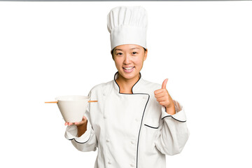 Wall Mural - Young chef asian woman holding a bowl of ramen isolated smiling and raising thumb up