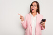 © Asier - Business caucasian woman holding a mobile phone isolated on white background smiling and pointing aside, showing something at blank space.
