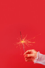 Wall Mural - Bengal fire in female hand on red background. Minimalistic christmas festive concept vertical format