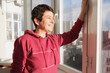 © Galina - Middle-aged brunette woman stands on the glazed balcony of her apartment and and smiles. Housewarming in a multi-storey building. Satisfied apartment owner.