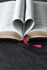 Wall Mural - Open Holy Bible Book with golden pages folded in a heart shape on dark background with copy space. Vertical shot. Christian biblical concept of love and faith.