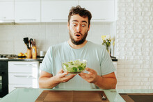  Man Grimaces Very Expressively At The Sight Of A Salad Of Greens, Holding A Bowl In His Hands. He Looks At The Vegetables With Wide Eyes And Does Not Want To Eat Them. Stop Diet. Wants To Be Happy. 