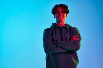 Portrait of young man with curly hair posing in casual clothes, smiling isolated over blue background in neon light