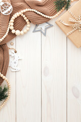 Christmas vertical background with brown woolen sweater, wooden garland, gift box, vintage decorations on old white wood table planks