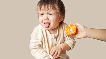 a baby, child with a food allergy doesn't want to eat sour orange, winces, the baby refused to eat vitamins , he made a grimace and stick out his tongue