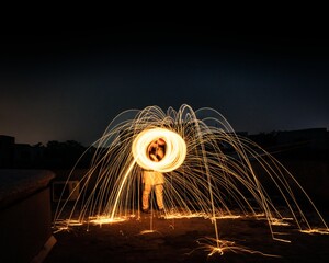 Wall Mural - Man spinning a ball of burning steel wool under a dark clear sky