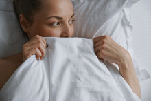 Woman Relaxing And Peering Over The Top Of Bed Sheet