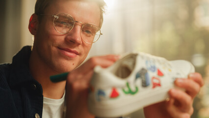 Aufkleber - Close Up Portrait of Satisfied Male Artist Refreshing Sneakers by Painting on Them in his Loft Flat. Talented and Creative Man Making Custom Made Design for Shoes. Millennial People Concept.