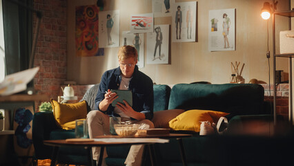 Aufkleber - Caucasian Male Designer Draws on Digital Tablet, while Sitting on Sofa in Relaxed Position. Loft Apartment Stylish Living Room. Smart People and New Generation Professionals Concept.