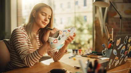 Leinwandbilder - Full of Ideas Female Fashion Designer Creating and Designing Used Pair of Sneakers. Teenager Artist Looking at Laptop and Drawing on Shoes. Custom Made and Eco Friendly Clothes Concept.