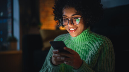 Aufkleber - Cinematic Portrait of Black Female with Curly Hair Sitting on the Floor at Home and Using Smartphone. Diverse Woman Receives Good News and Chatting with Friends Via Social Media.