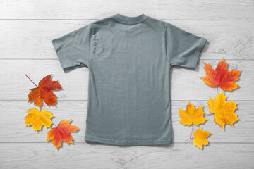 Wall Mural - Back view of boys t-shirt on white wooden table background with autumn leaves top view. Mockup for design close up
