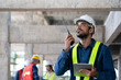 © PINA - maintenance manager using walkie-talkie to communicate safety and quality control policy with workers on site, civil engineer informs infrastructure and building construction progress to supervisor