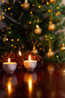 © Angela - Decoração de Natal. Algumas velas acesas em uma superfície refletiva e um detalhe desfocado da árvore de Natal ao fundo.