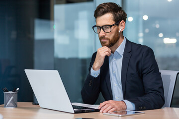 Wall Mural - Senior businessman in glasses and beard is thinking about a decision, man is working inside the office and using laptop at work, mature investor in a business suit is sitting at the table