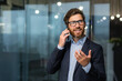 © Liubomir - Mature businessman in a business suit talking on the phone, the manager is satisfied with the result of the achievement and work talks about the positive result, the man is at work inside the office.