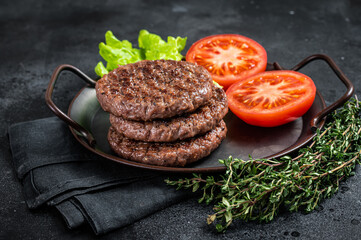 Wall Mural - Tasty grilled burger beef patty with tomato, spices and lettuce in kitchen tray. Black background. Top view