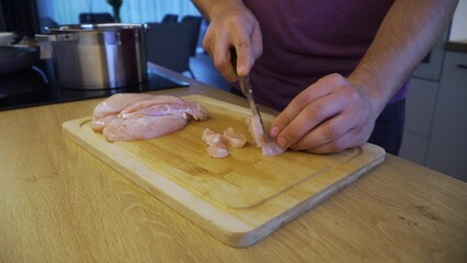 Wall Mural - Man is chopping chicken breasts on the wooden board in the kitchen,with a saucepan in the background