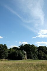 Wall Mural - Vertical shot of a gazebo between green trees in the meadow under blue cloudy sky