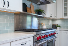 Kitchen Detail Of Large Stove With Red Knobs, Pale Green Tile Backsplash And Wooden Kitchen Accessories.