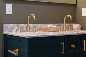 Modern bathroom vanity details of gold faucets and hardware with marble counter, dark blue cabinets and decorative gold trim mirror.