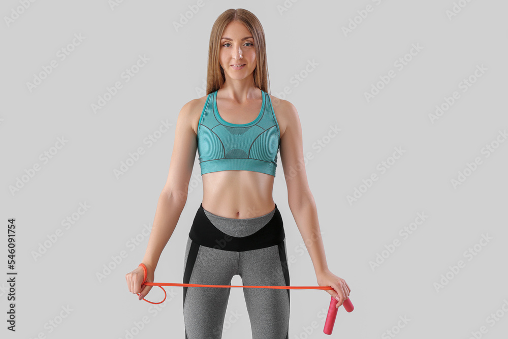 Sporty young woman with jumping rope on light background