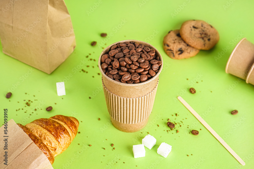 Paper cup of coffee beans on green background