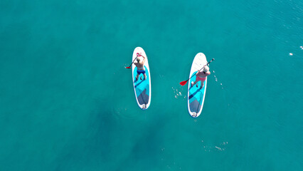 Aerial drone photo of two women practising Stand Up Paddle board or SUP surf in tropical exotic island bay with emerald crystal clear sea