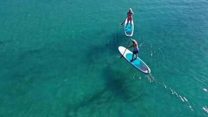 Aerial drone photo of two women practising Stand Up Paddle board or SUP surf in tropical exotic island bay with emerald crystal clear sea