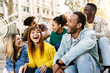 © Xavier Lorenzo - Young group of hispanic latin friends having fun together outdoors. Millennial multiracial people laughing while social gathering sitting on stairs at city street