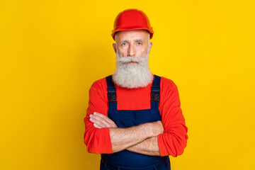 Wall Mural - Photo of serious confident senior guy dressed uniform overall red hardhat arms crossed isolated yellow color background