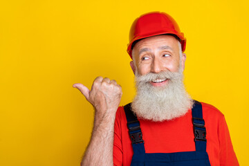 Wall Mural - Photo of positive dreamy age man workwear overall red hard hat looking pointing thumb empty space isolated yellow color background