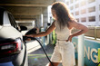 © Cavan Images - Happy woman plugging in cable while charging electric car at station