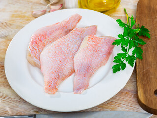 Raw fish with condiments, red perch fillet on plate with garlic and parsley on wooden surface