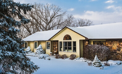 View of traditional suburban Midwestern house and front yard in winter after snowstorm; blue sky with clouds in background