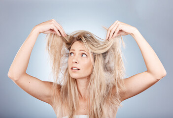 Hair care, stress and woman sad about frizz, split ends and messy style against a grey studio background. Frustrated, unhappy and angry model with problem with her hair, frustration and worry