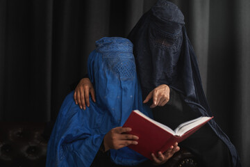 afghan muslim women with burka traditional costume, reading holy quran against the dark background