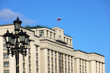 Wall Mural - Parliament building in Moscow with Russian flag on background of blue sky. Facade of State Duma of Russia with soviet coat of arms, russian authority